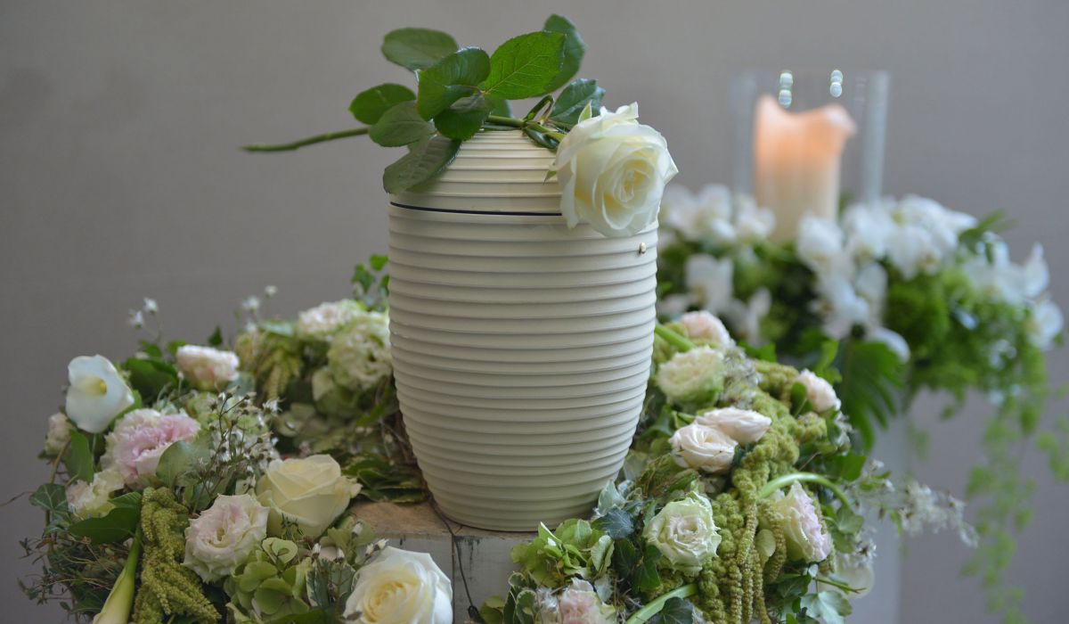 Schön dekorierte weiße Urne mit gestecktem Blumenkranz aus hellen und roséfarben Rosen