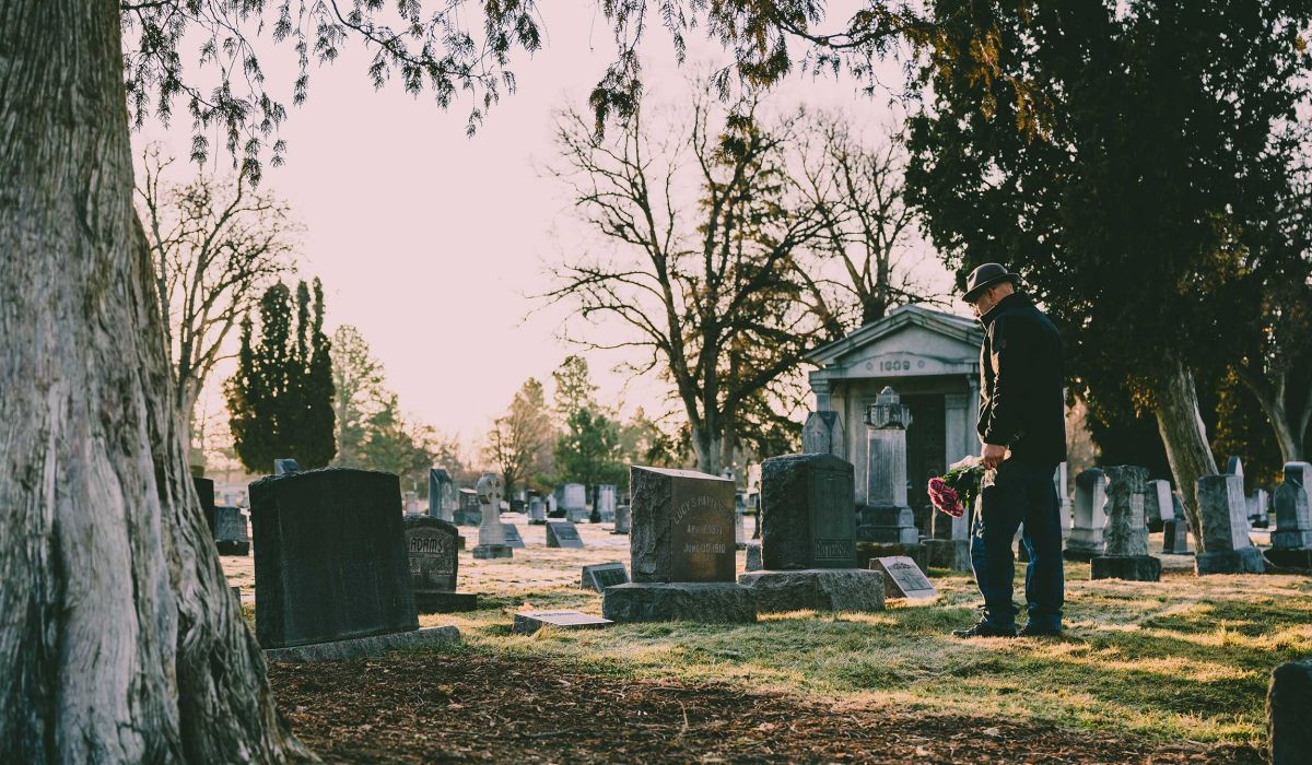 Angehöriger mit einem Blumenstrauß in der Hand auf einem Friedhof