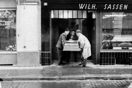 Schwarz-Weiß Bild drei Sargträger tragen einen Sarg aus dem Ladenlokal von Wilhelm Sassen